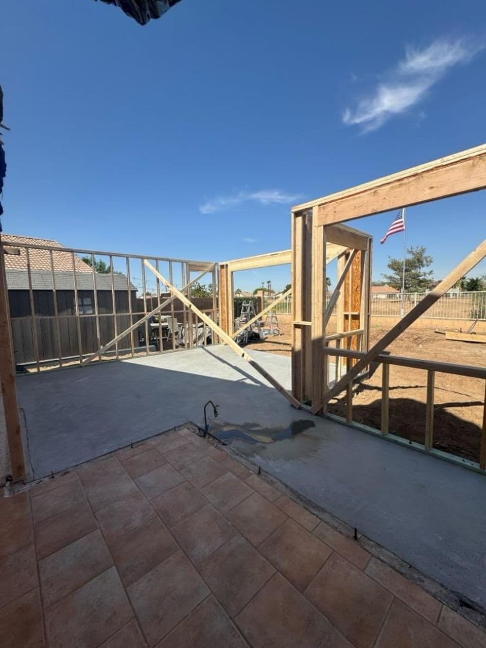 Construction site showing wooden frame, concrete floor, and American flag in the background.
