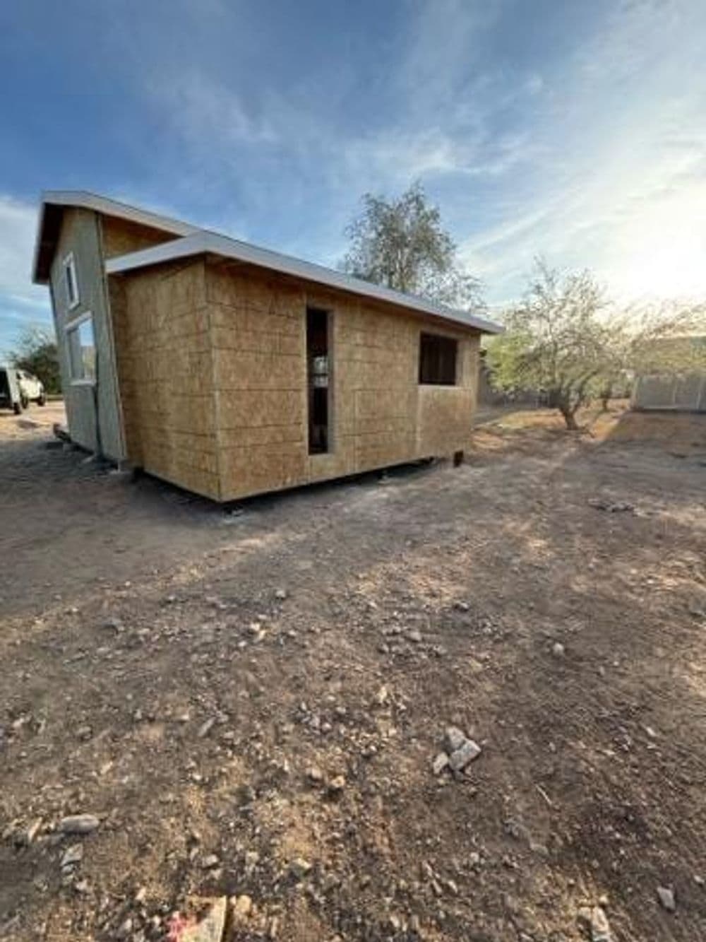 Newly constructed small wooden cabin in a rural setting, surrounded by gravel and sparse vegetation.