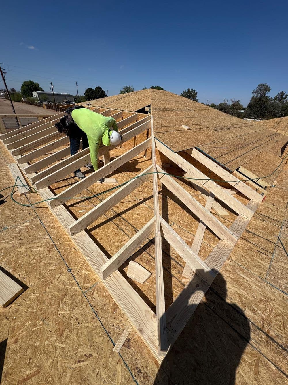 Roofing construction with a worker installing wooden trusses on a sunny day.