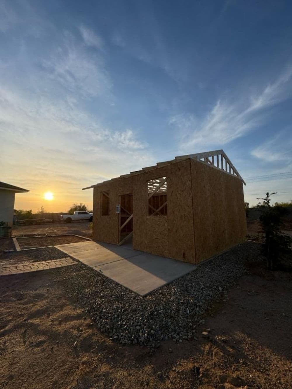 Newly constructed wooden house at sunset with clear sky and gravel pathway.