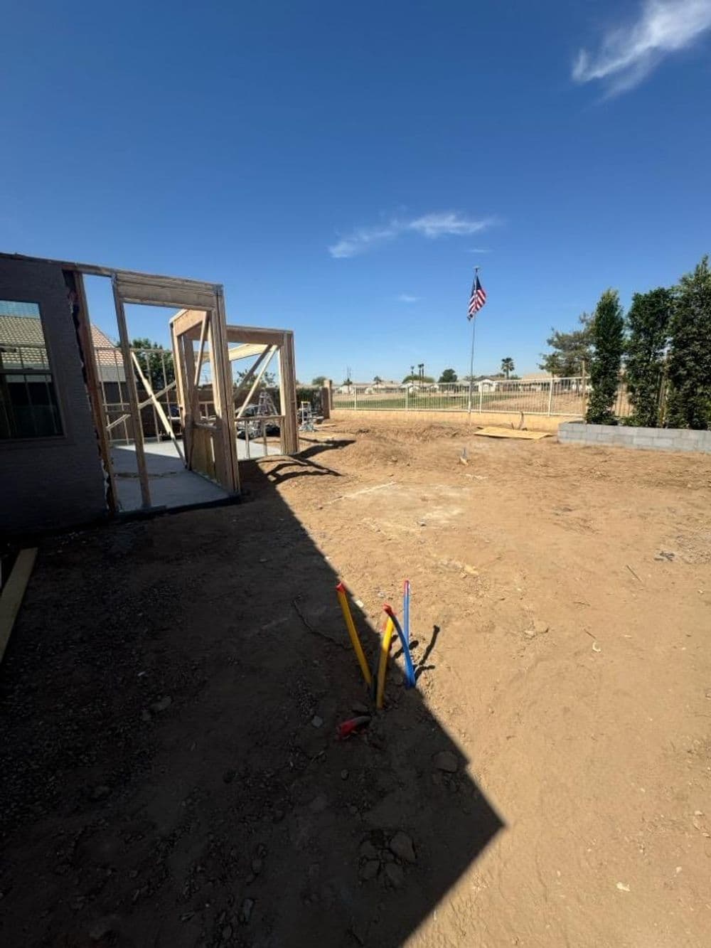 Construction site with framing, tools, and American flag against a clear blue sky.
