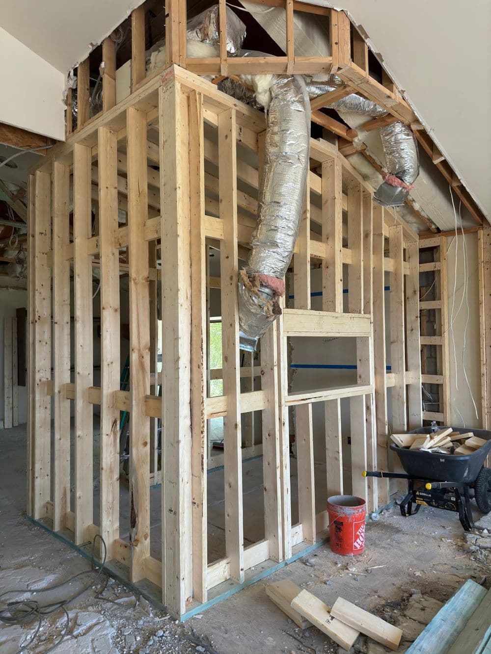 Framed wall under construction with insulation and tools in an unfinished interior space.