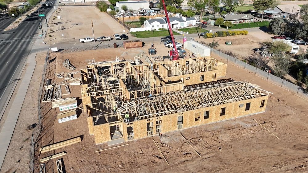 Aerial view of a construction site with framed building structure and nearby vehicles.