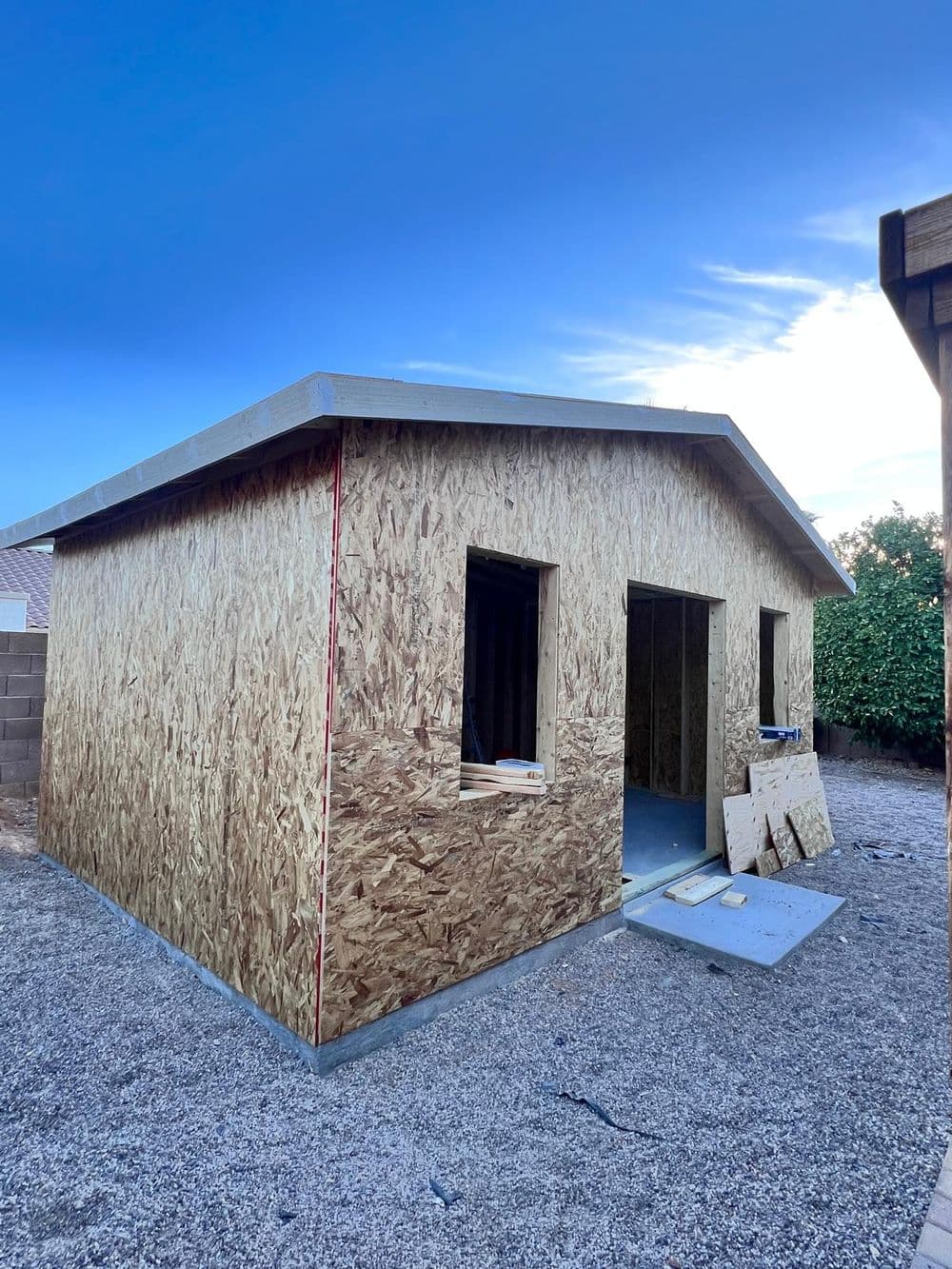 Newly constructed wooden house with OSB exterior, unfinished windows, and gravel foundation.