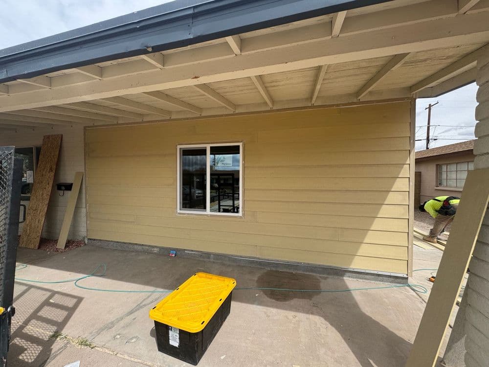 Home exterior with freshly painted yellow siding and a large window, tools and materials nearby.