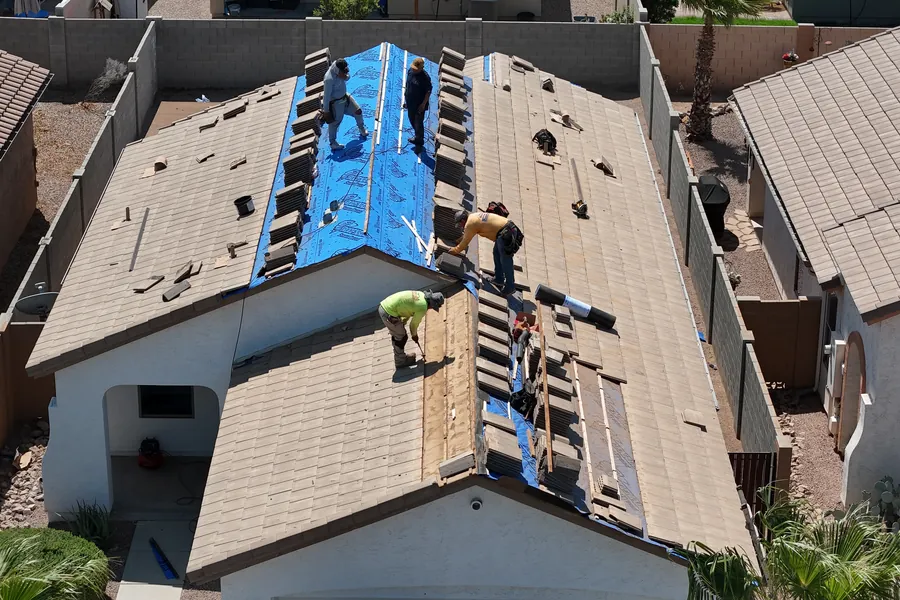 A roofing crew stripping and re-covering a house roof, seen from above with the underlayment down