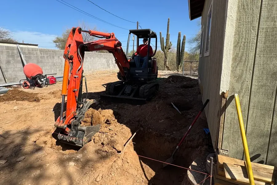 A compact excavator cutting footings alongside an existing house