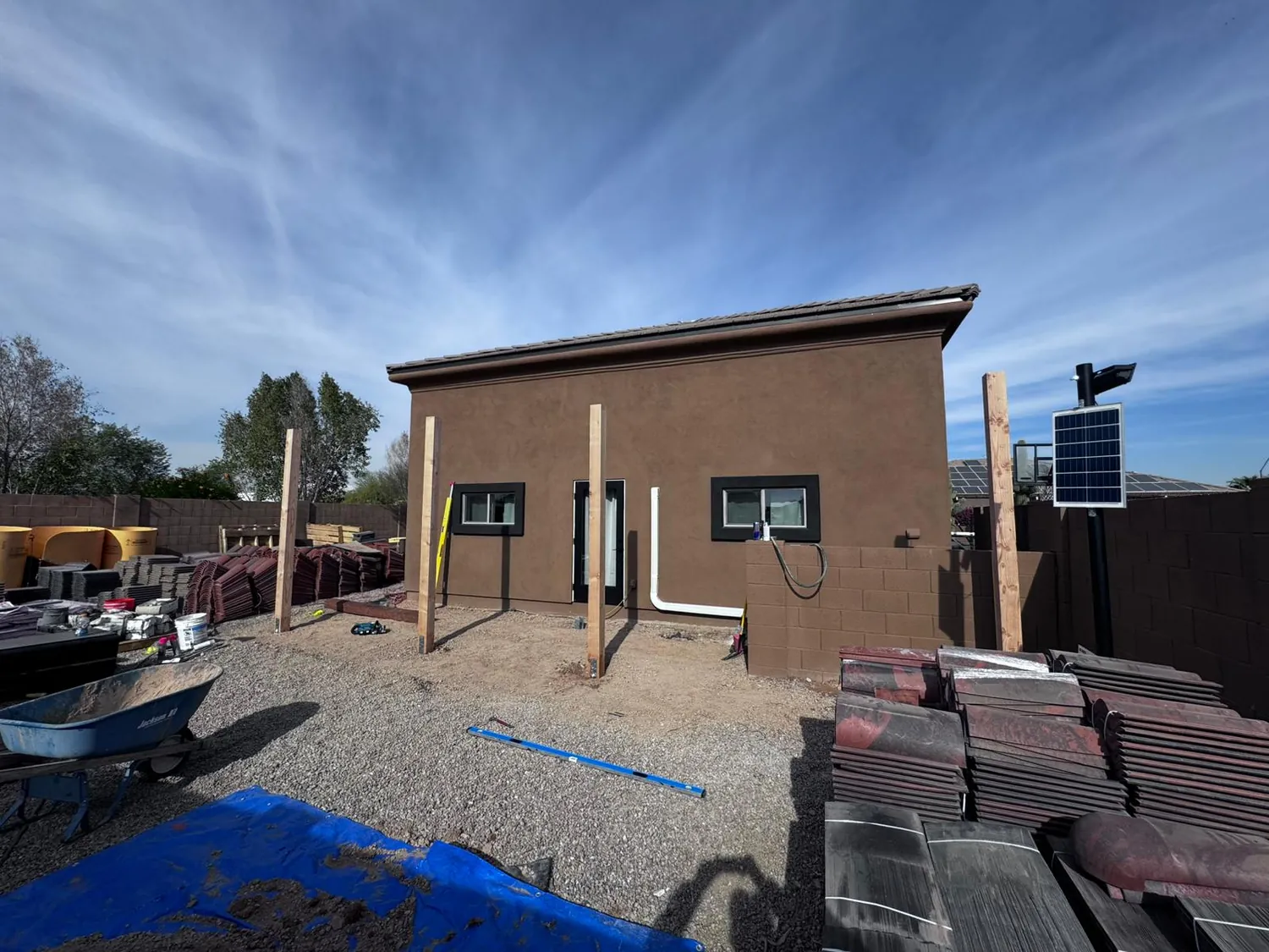 A finished casita with stucco walls, a tile roof and windows set, with roof tile stacked alongside