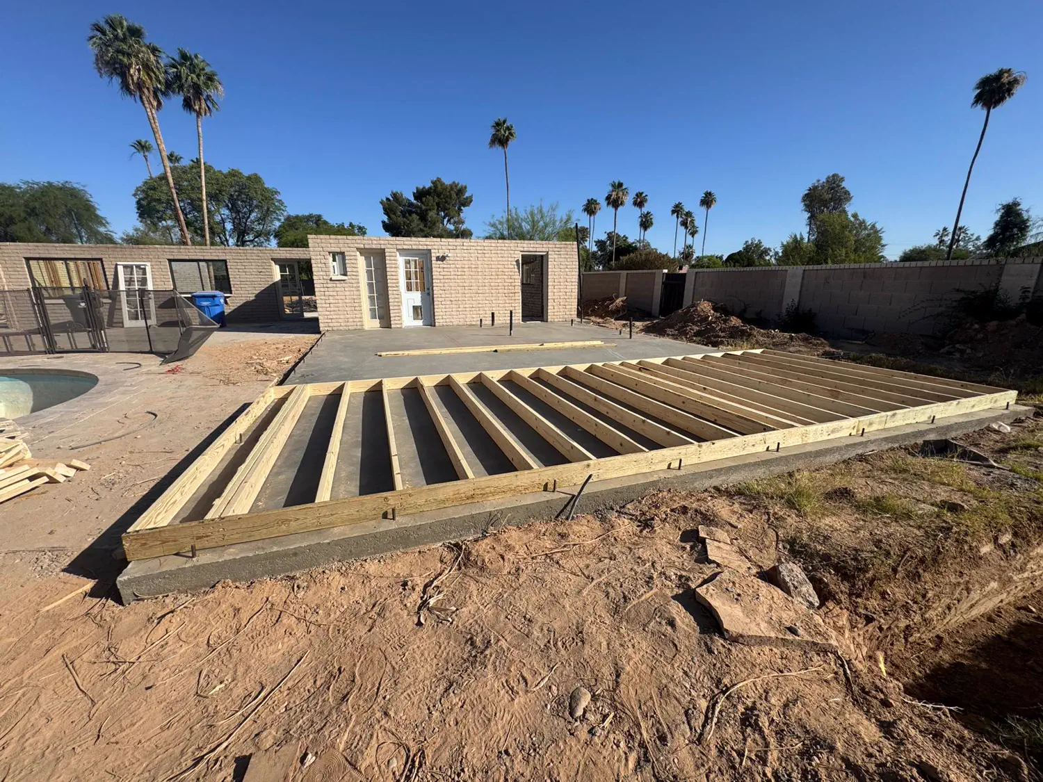 Deck framing and joists laid out on grade beside a pool