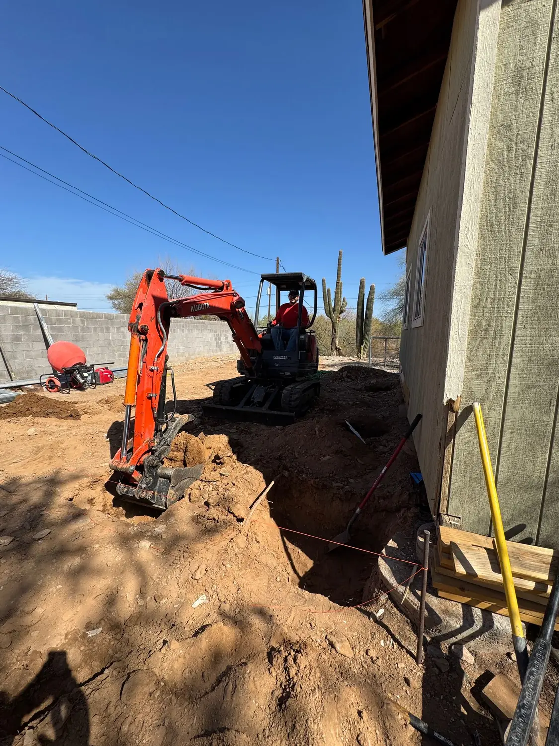 A compact excavator cutting footings alongside an existing house