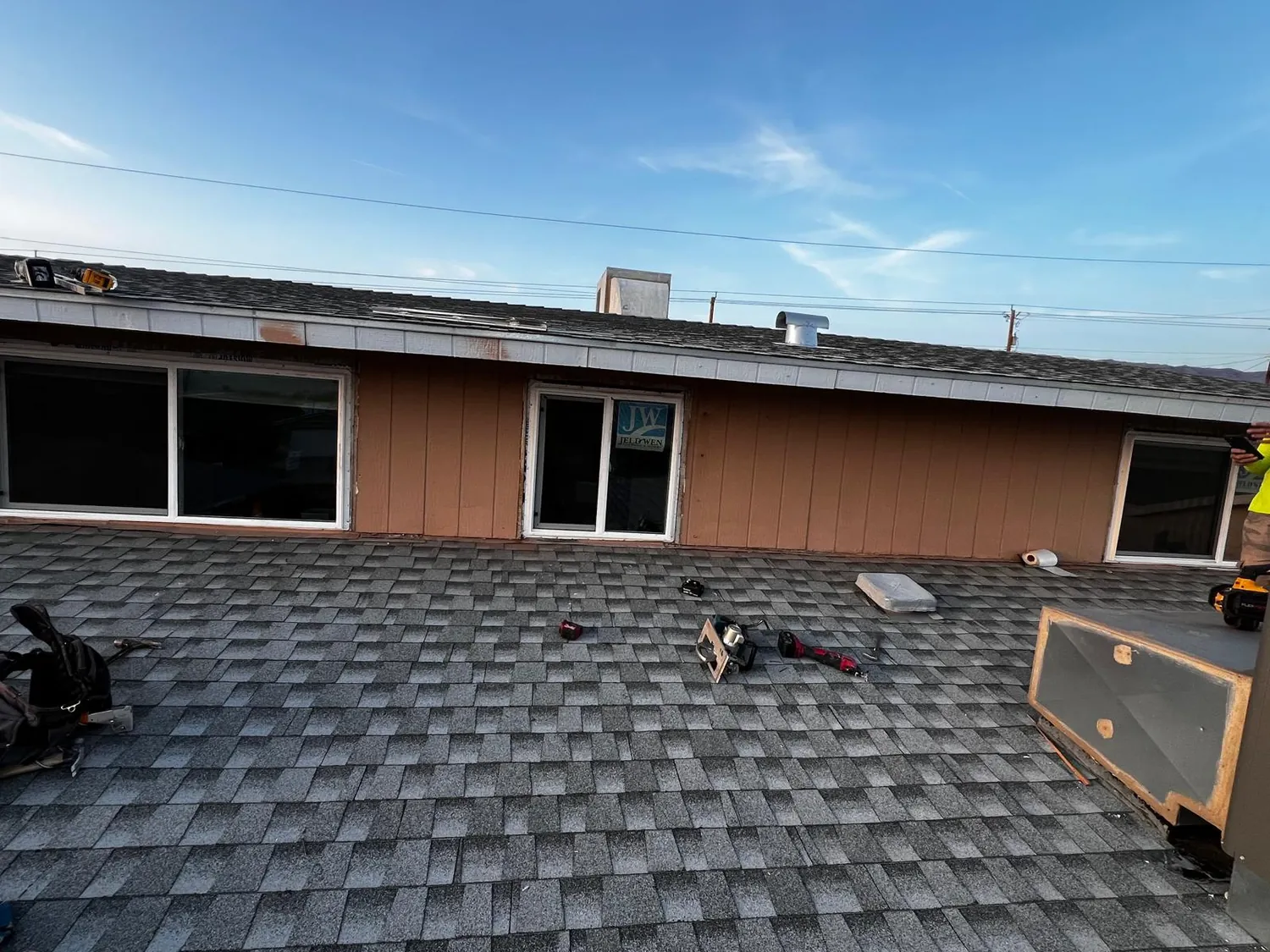 A newly shingled roof with the tools still out and new windows going in behind it