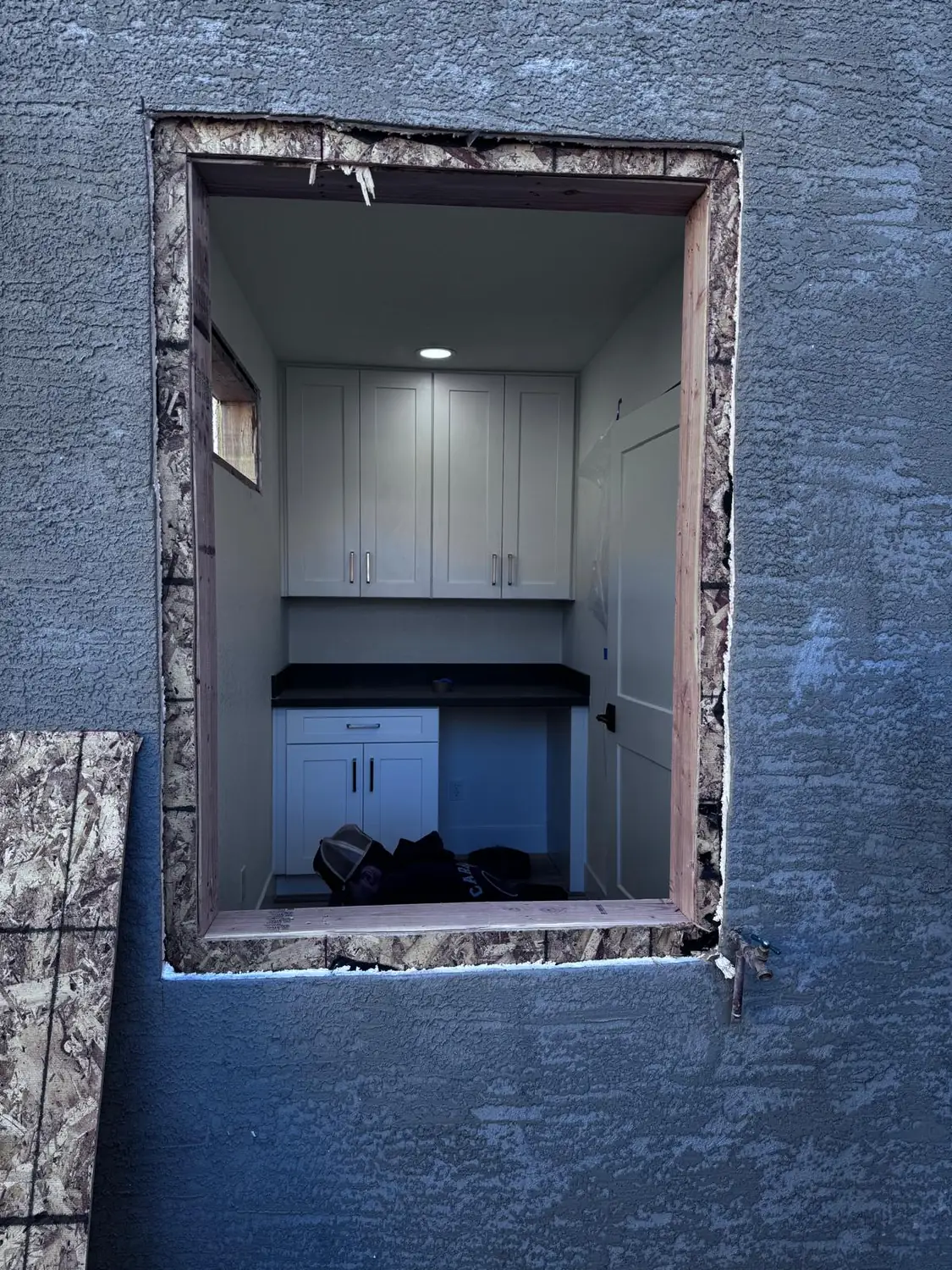An opening cut through a stucco wall for a new window, the finished room visible inside