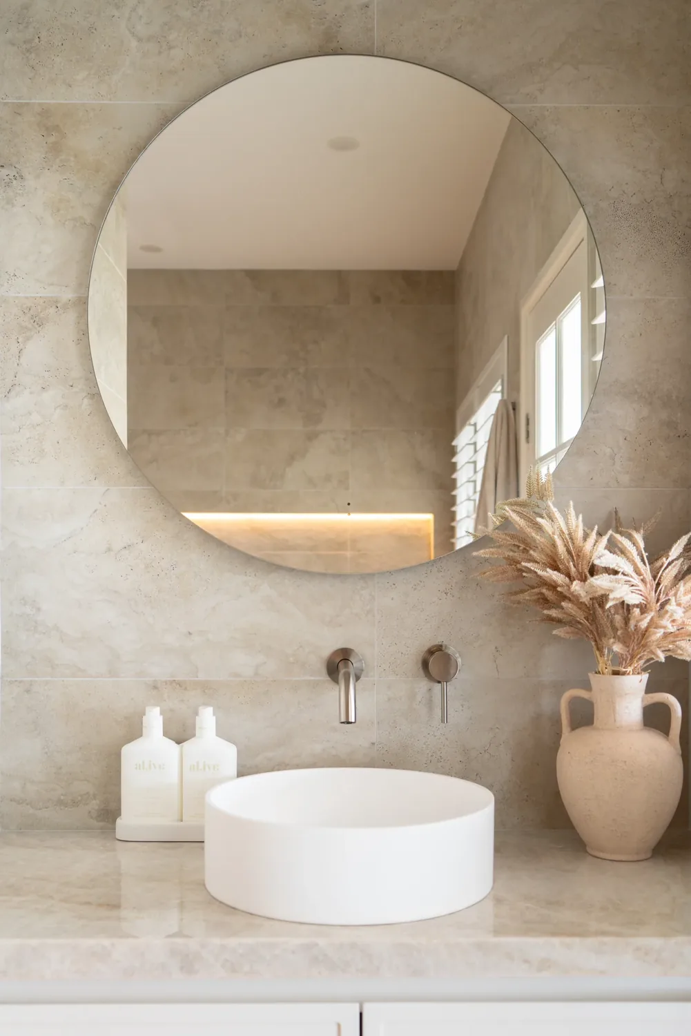 A finished bathroom with a round mirror and a basin on a stone top